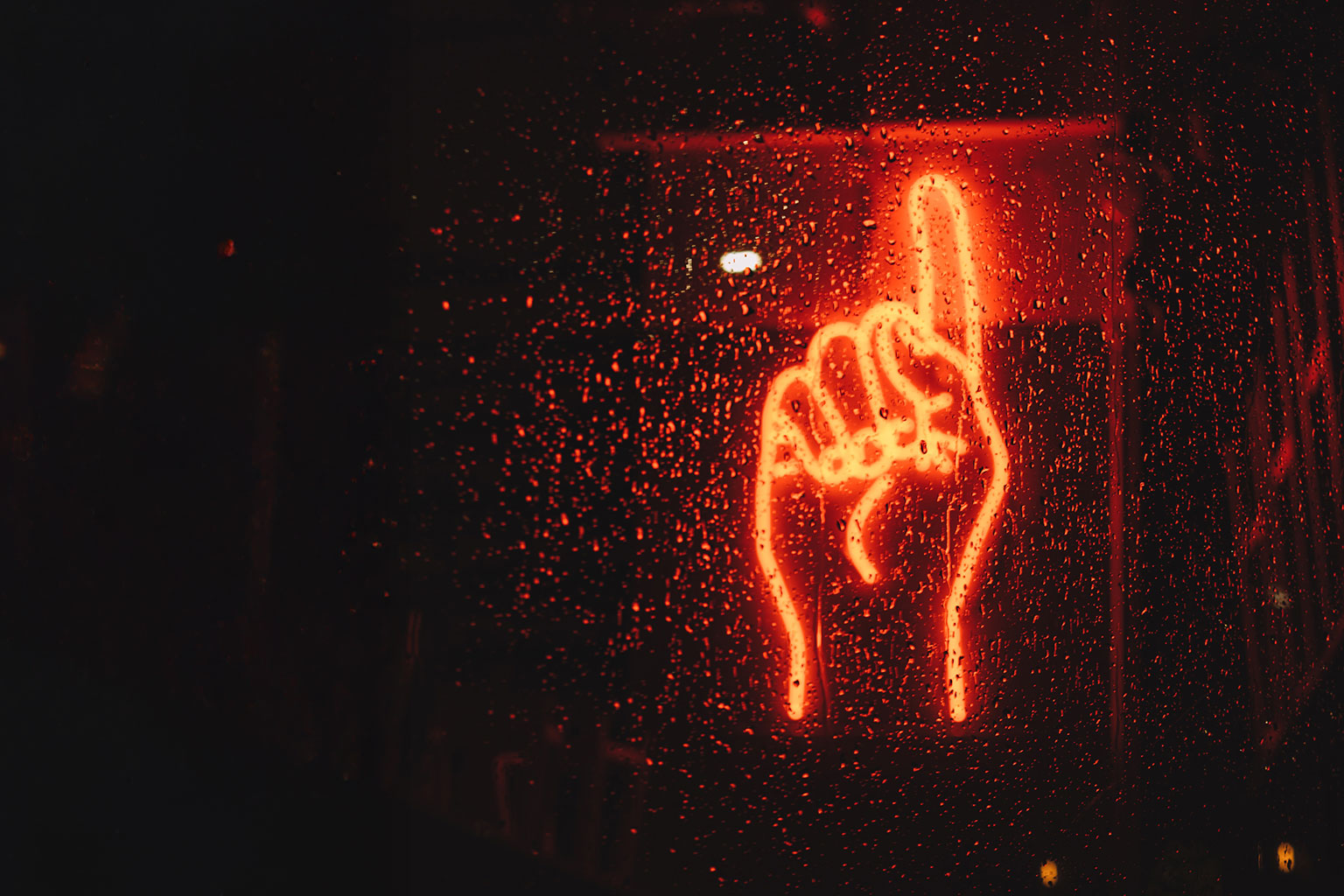 Erhobener Zeigefinger als Neon-Schild im Dunkeln