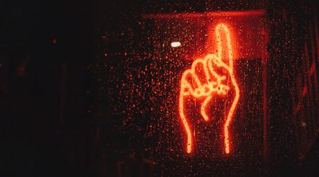 Erhobener Zeigefinger als Neon-Schild im Dunkeln